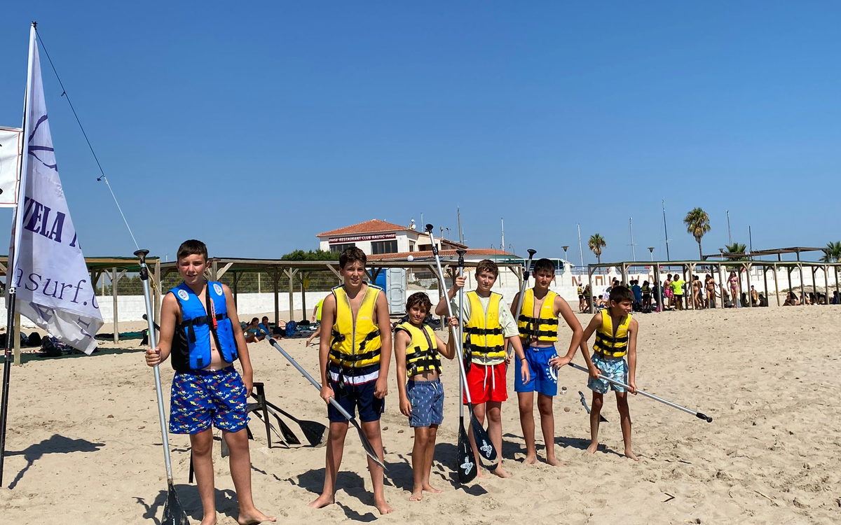 Chicos de 12 a 14 años con chaleco y palas de paddle surf en la orilla